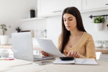 İş konsepti. Odaklanmış kadın muhasebesi, finansal rapor ve bankacılık yatırımı için gelir ve giderlerin hesaplanması, mutfakta dizüstü bilgisayar kullanımı