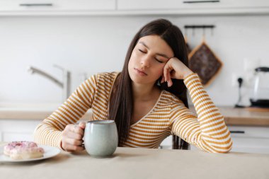 Uykulu bayan yorgun hissediyor, mutfakta masada oturuyor ve kahve içiyor, uykusuzluk ve uykusuzluk çekiyor.