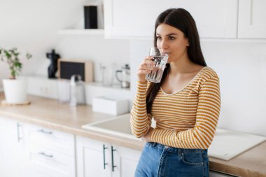 Hidrasyon konsepti. Bayan, ferahlatıcı su içiyor. Mutfağın içinde duruyor. Sabahları vücudunu suluyor.