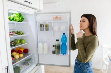 Buzdolabının önünde durmuş, yüzünde dalgın bir ifade olan genç bir kadın kahvaltı yapmayı düşünüyor.