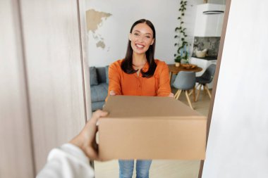 Teslimat konsepti. Heyecanlı bayan müşteri kuryeden bir kutu alıyor, evinin kapısında dikiliyor ve kameraya gülümsüyor.