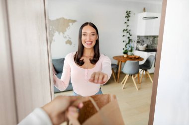 Alışveriş teslimatı. Kurye, mutlu kadın müşteriye alışveriş çantası veriyor. Evinin kapısında bekliyor.