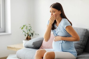 Hamilelik sabah bulantısı. Hamile kadın mide bulantısı çekiyor. Kanepede otururken kendini kötü hissediyor.