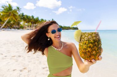 Mutlu kadın plajda taze ananasın tadını çıkarıyor, tropikal bir ortamda. Yaz zamanı neşe ve heyecan