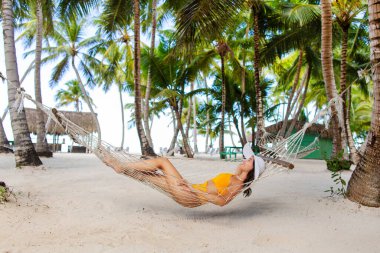 Genç kadın hamakta sallanırken güneşleniyor palmiye ağaçlarının arasında, egzotik tropik tatilin tadını çıkarıyor.