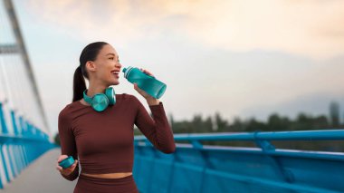 Koştuktan ve açık havada antrenman yaptıktan sonra deniz kenarındaki gezinti alanında dinlenen ve içen Avrupalı bir kadın, panorama, kopyalama alanı