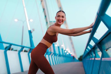 Antrenmandan sonra mola veren heyecanlı bayan, eğitimi sırasında köprüde duruyor, dinleniyor, yan bakıyor ve gülümsüyor.