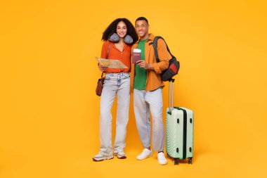 Harita, pasaport ve biletlerle sarı arka planda bavullarıyla poz veren Afro-Amerikan çift. Seyahat hazırlığı, tatil planlama kavramı