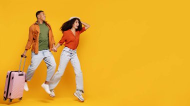 Tatile hazırım. Sarı arka planda bavulla koşan mutlu Latin çift, eşleri el ele tutuşuyor ve fotokopi odasına bakıyor.