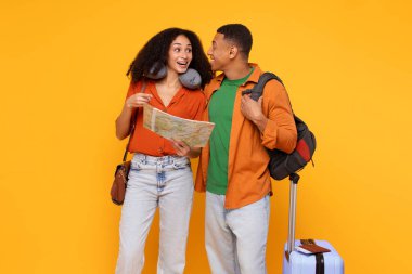 Seyahat yeri seçimi. Mutlu Latin çift ellerinde harita, birbirlerine gülümsüyorlar, tatillerini yurtdışında planlıyorlar, sarı arka planda duruyorlar.