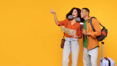 Mutlu Latin eşler tatile hazır, bavulları ve seyahat haritalarıyla fotokopi alanını gösteriyorlar, sarı arka planda duruyorlar.