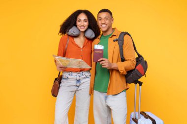 Tatile hazırım. Mutlu Latin çift elinde harita ve pasaport, seyahat yastığı olan kadın, sırt çantalı adam, tatil macerasına hazır olduklarını gösteriyor, sarı arka plan.