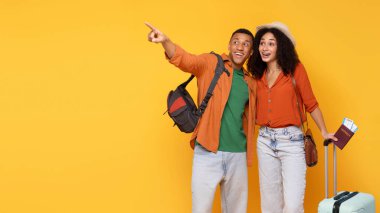 Trip reklamı. Heyecanlı siyah çift kucaklaşıyor, fotokopi alanına işaret ediyor, sarı arka planda seyahat için yer gösteriyor, panorama