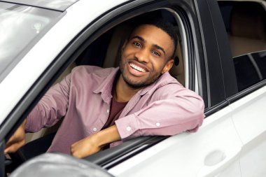 Beyaz camlı ve kameraya gülümseyen, yeni araba kiralayan veya alan mutlu Afrikalı Amerikalı adam.