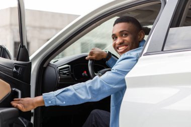 Pozitif siyah adam arabadan çıkıyor, otomobil kapısını açıyor ve gülümsüyor, içeri giriyor. Otomatik test sürüşü, satın alma, kiralama kavramı