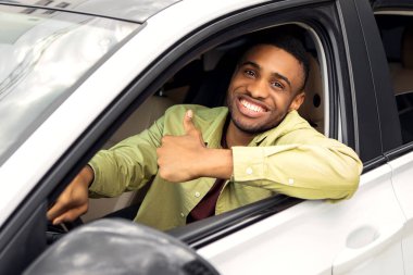 Mutlu Afrikalı Amerikalı adam onayını veriyor, test sürüşünden sonra yeni bir otomobilde oturuyor, araç alıyor, pencereden dışarı bakıyor ve gülümsüyor.