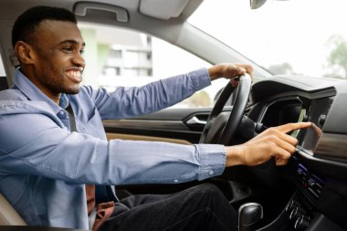 Ulaşım ve modern teknoloji konsepti. Neşeli siyah adam, araç gösterge panelindeki navigasyon sistemini kullanarak rota arıyor.