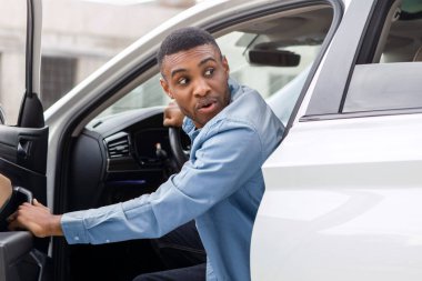 Korkmuş siyah adam arabasının kapısını açtı ve şok olmuş yüz ifadesiyle geriye baktı.