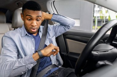 Trafikte sıkıştım. Stresli siyah adam sürücü koltuğunda oturuyor, kolundaki saate bakıyor ve kafasına dokunuyor, geç kalıyor.