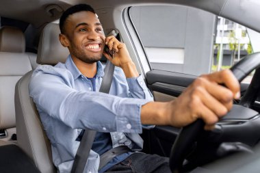 Mutlu Afrikalı Amerikalı sürücü araba kullanırken telefonla konuşuyor, içeride oturuyor, direksiyon başında oturuyor ve telefonla konuşuyor.