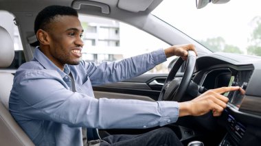 Ulaşım ve modern teknoloji konsepti. Neşeli siyah adam, araç gösterge panelindeki navigasyon sistemini kullanarak rota arıyor.