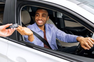 Neşeli siyah adam güzel bir arabanın içinde oturuyor ve araba anahtarını kiralıyor.