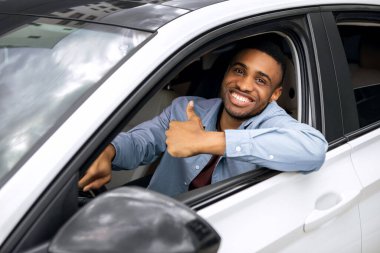 Mutlu Afrikalı Amerikalı adam onayını veriyor, test sürüşünden sonra yeni bir otomobilde oturuyor, araç alıyor, pencereden dışarı bakıyor ve gülümsüyor.