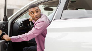 Korkmuş siyah adam arabasının kapısını açtı ve şok olmuş yüz ifadesiyle geriye baktı.