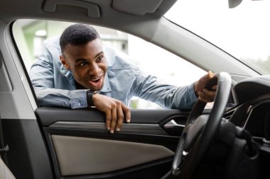 Heyecanlı siyah adam yeni arabanın camından bakıyor, satın almadan önce kontrol ediyor, adam araba alıyor ya da kiralıyor.