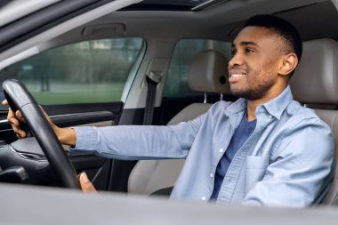 Yeni otomobilin test sürüşü. Sürücü koltuğunda oturan Afro-Amerikalı adam, açık pencereden yandan çekilmiş.