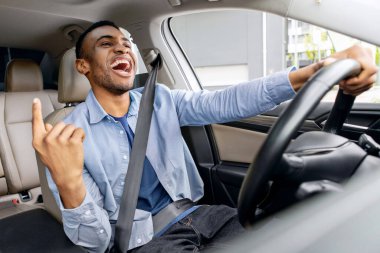 Duygusal siyahi adam araba sürerken eğleniyor, müzik dinliyor ve şarkı söylüyor, elini hareket ettiriyor, içeriden vuruluyor.