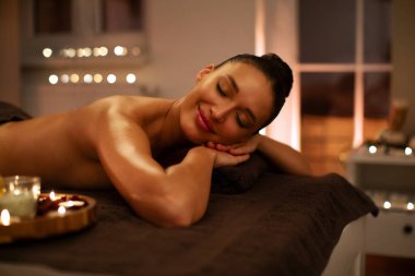 Genç ve rahat bir bayan spa salonunda aromaterapi tabağının yanında uzanıyor ve atmosferin tadını çıkarıyor. Vücut masajı konsepti