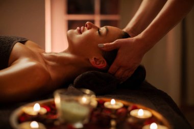 Rahat kadın, yanında aroma mumları ve yan görüş eşliğinde sıcacık spa atmosferinde yüz ve kafa masajı yaptırmaktan hoşlanıyor.