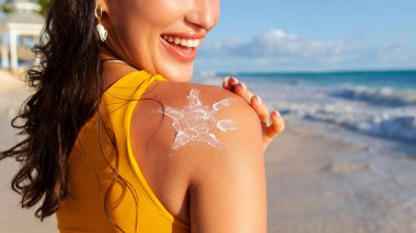 Vücut güneş koruyucu güneş kremi. Omzuna güneş kremi süren bir kadın, sahilde okyanus kıyısında poz veren, yakın plan, boş alan olan bir panorama