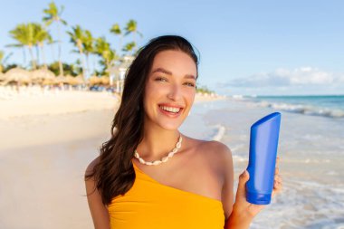 UV güneş ışınlarından korunma. Güneş kremi tutan mutlu Avrupalı kadın ya da tropik plaj arka planında losyon.