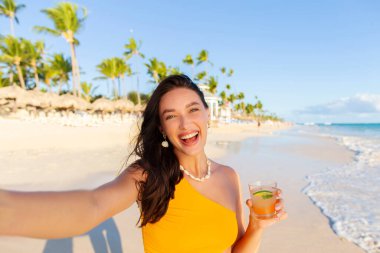 Heyecanlı bir kadın kokteyl içiyor ve sahilde eğleniyor. Okyanus kıyısında ya da tropik bir tatil köyünde yürürken mutlu oluyor.