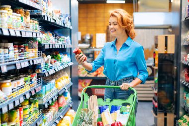 Markette ürünlere bakan, süpermarkette alışveriş yapan ve cam kavanozla ilgili bilgi okuyan mutlu bir kadın. Kadın kostümcü marketten yiyecek alıyor.
