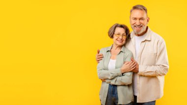 Emekli çifti sevmek, kucaklaşmak, son yıllarında sevgi ve mutluluk göstermek, sarı arka planda birlikte poz vermek.