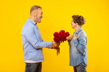 Sevgili Avrupalı koca sürpriz eşine bir buket çiçek veriyor. Romantik bir günü, doğum gününü, sarı arka planda yıldönümünü kutluyor.