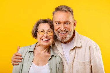 Sarı stüdyo arka planında poz veren, kameraya sarılıp gülümseyen son sınıf öğrencisi kadın ve erkeğin portresi. Mutlu evlilik ve emeklilik kavramı