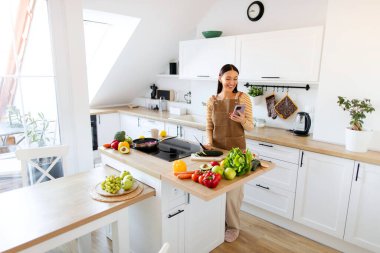 Kadın mutfakta dikilirken ve akşam yemeği için sebze salatası pişirirken akıllı telefon tarifi kullanıyor.