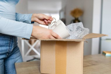 E- ticaret perakende satış sitesinden sipariş edilen paketleri açan ve bardakları tutan bir kadın. Yeni çanak çömlek konseptini alan memnun bayan müşteri.