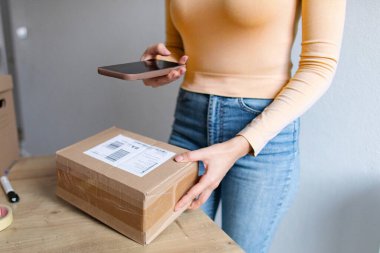 Kadın paketleri nakliye için hazırlıyor, bilgilerini akıllı telefon kullanarak belgeliyor, cep telefonu uygulaması kullanılarak paketlerin dağıtım sürecini izliyor