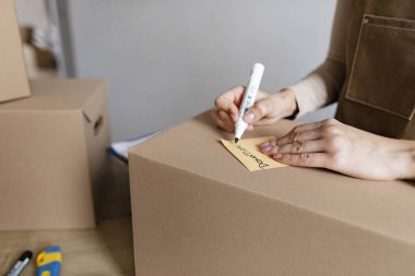 Genç bayan küçük işletme sahibi kutuya kelime bağışı yazıyor, nakliye ve teslimat için paket hazırlıyor, yakın çekim.