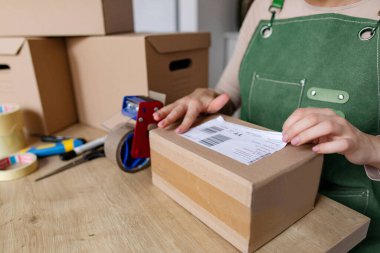 Genç girişimci kadın, paketlenmiş ürün kutusunun üstüne barkod etiketi yapıştırıyor, yakın çekim. Paket teslimatı, e-ticaret konsepti