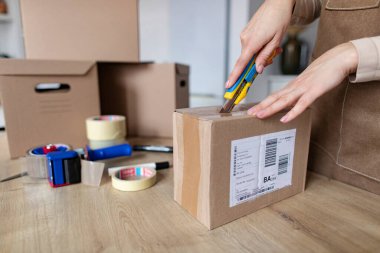 Kadın müşteri paket alıyor ve karton kutuyu kapalı bir masada açmak için bıçak kullanıyor. Yakın çekim.