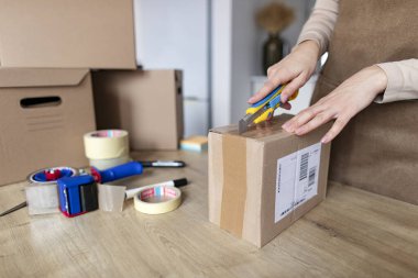 Kadın müşteri paket alıyor ve karton kutuyu kapalı bir masada açmak için bıçak kullanıyor. Yakın çekim.
