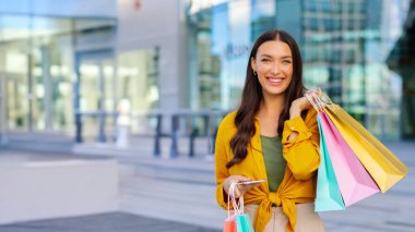 Mobil alışveriş uygulaması. Başarılı bir alışveriş yaptıktan sonra elinde akıllı telefon ve alışveriş torbaları tutan heyecanlı bir bayan. Alışveriş ve ecommerce