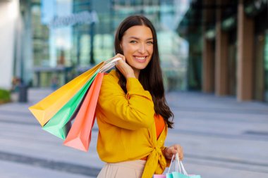 Mevsimlik satışlar. Bir sürü alışveriş çantası tutan ve kameraya gülümseyen mutlu kadın, alışveriş merkezinin yakınındaki şehir alanında yürüyor.