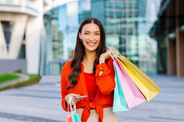 Mobil alışveriş uygulaması. Başarılı bir alışveriş yaptıktan sonra elinde akıllı telefon ve alışveriş torbaları tutan heyecanlı bir bayan. Alışveriş ve ecommerce